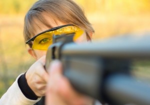 A young girl with a gun for trap shooting and shooting glasses aiming at a target