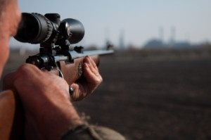 Hunter aiming with sniper rifle in the field